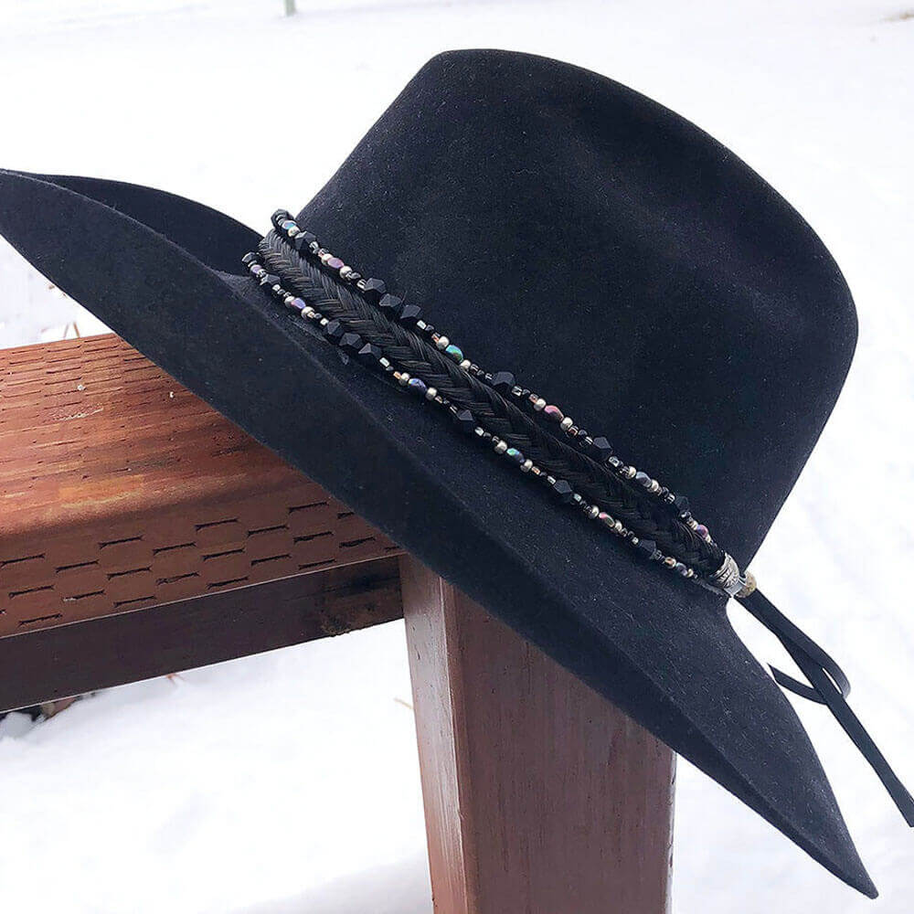 A black hat with a decorative triple strand hatband featuring a braid of horse hair, glass tubes, cones, and pearls, leather tassels, and sunburst conchos.