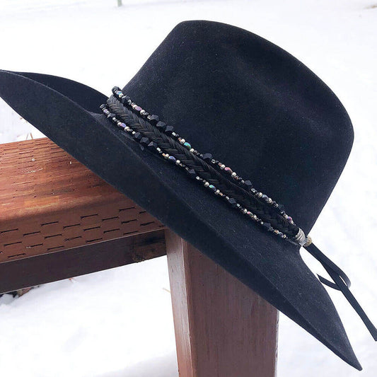 A black hat with a decorative triple strand hatband featuring a braid of horse hair, glass tubes, cones, and pearls, leather tassels, and sunburst conchos.